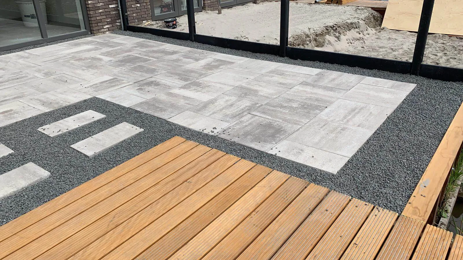 Terras met hardhouten vlonder en siergrind naast keramische tegels